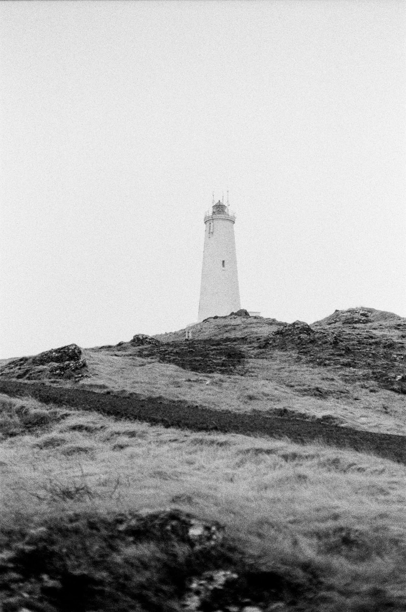 A lighthouse stands on a grassy hill.